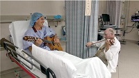 Dr. Sloan playing violin while patient in bed plays guitar